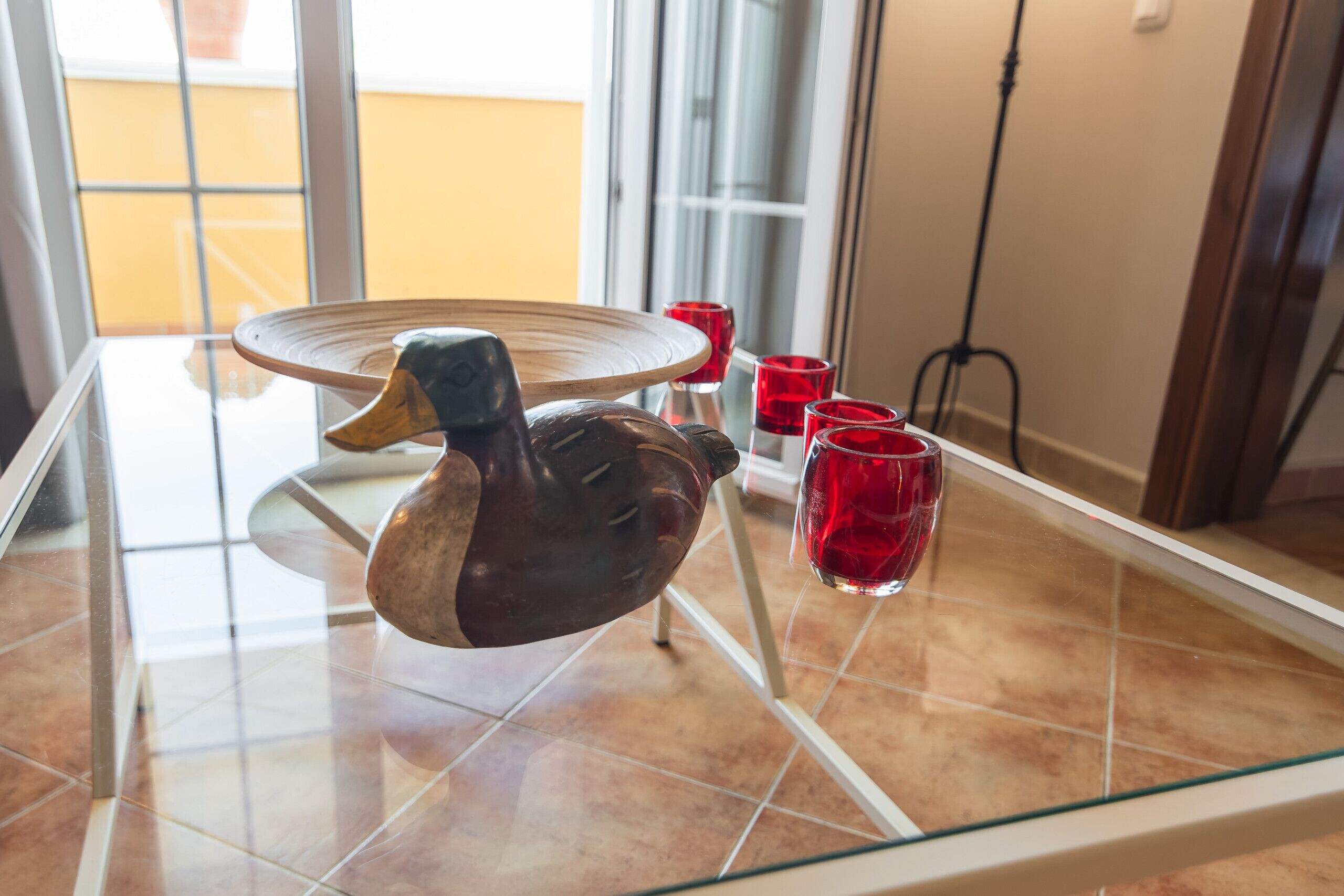 A glass table with a duck-shaped centerpiece, red glasses, and a tiled floor.