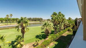 A golf course with a pond, palm trees, and a building with a balcony.