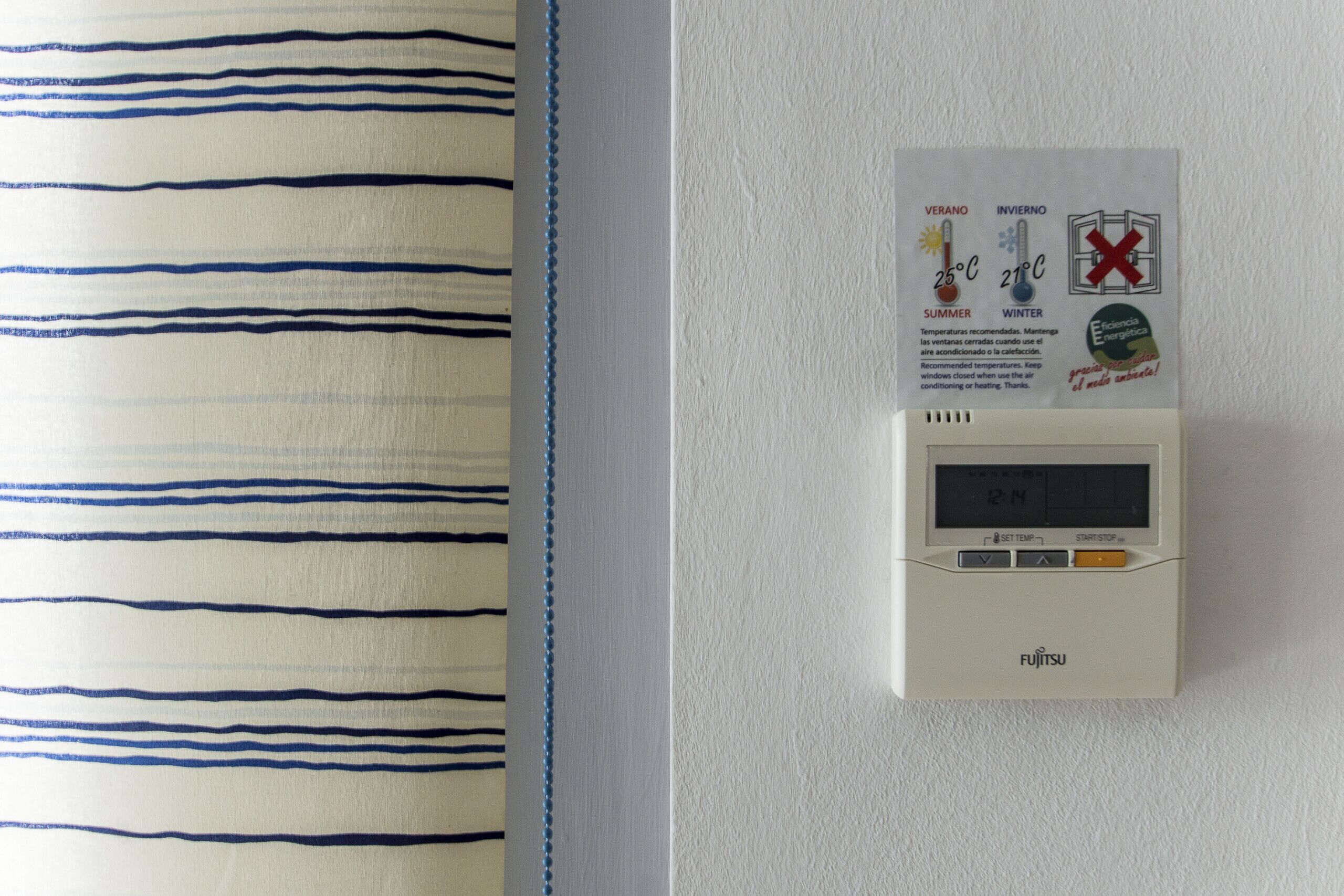 Un thermostat mural doté d’un affichage de la température et de boutons de contrôle, placé à côté d’un tissu à rayures.