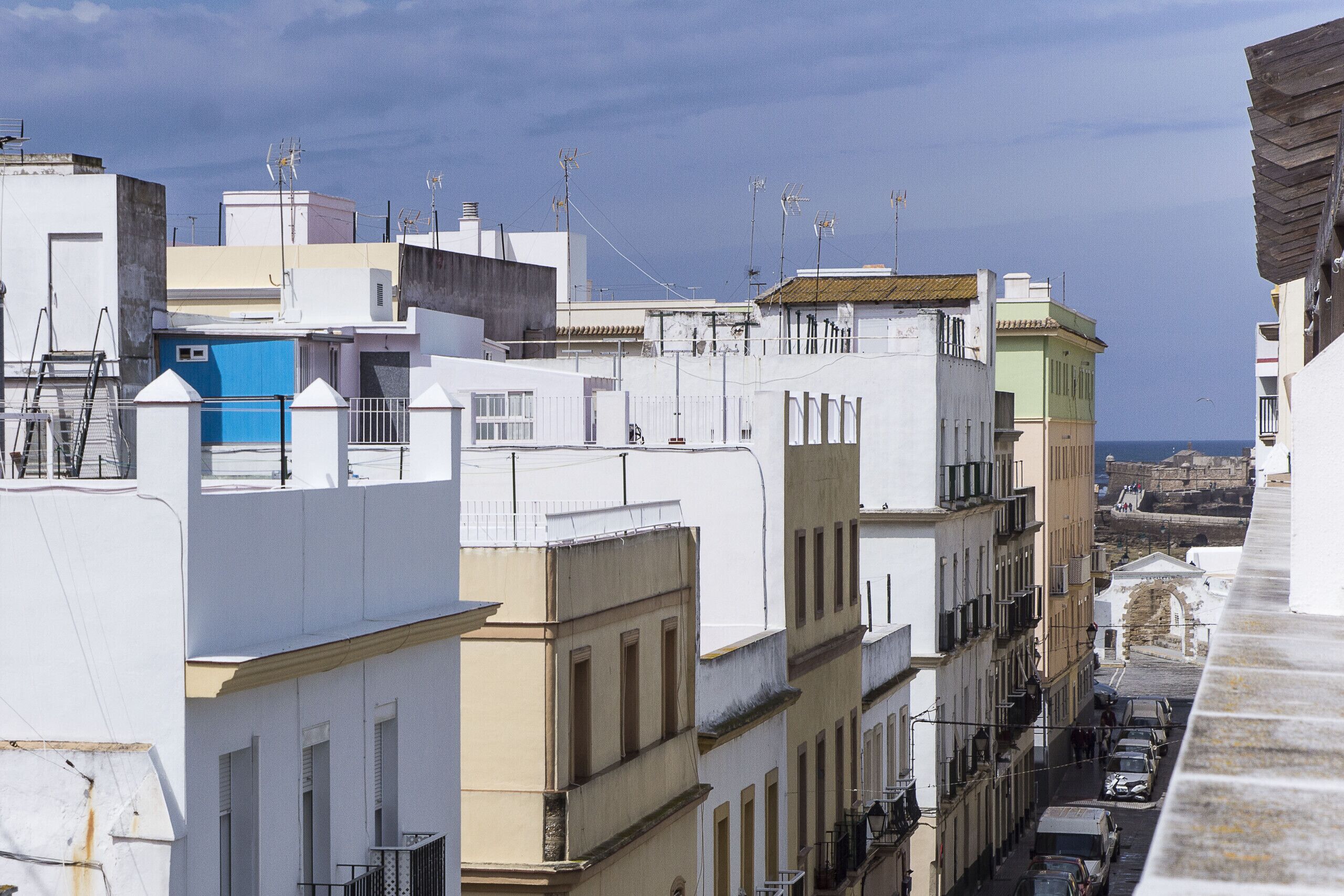 A narrow street lined with multi-story buildings, some with balconies and satellite dishes.