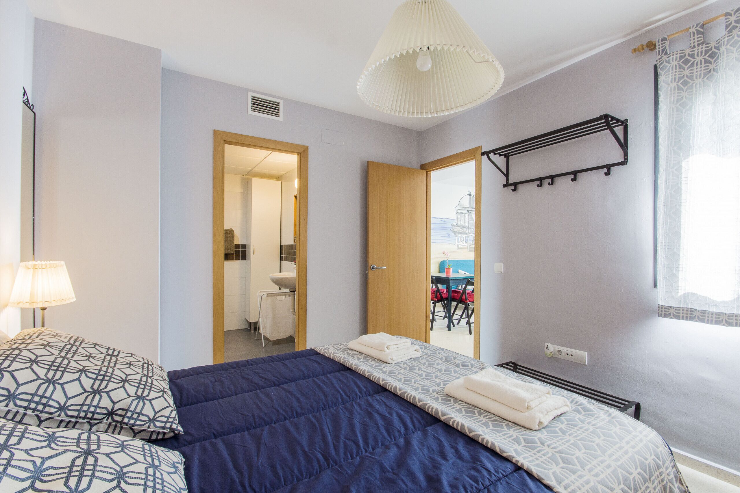 A bedroom with a large bed, a bedside table, a lamp, and a view of the outside.