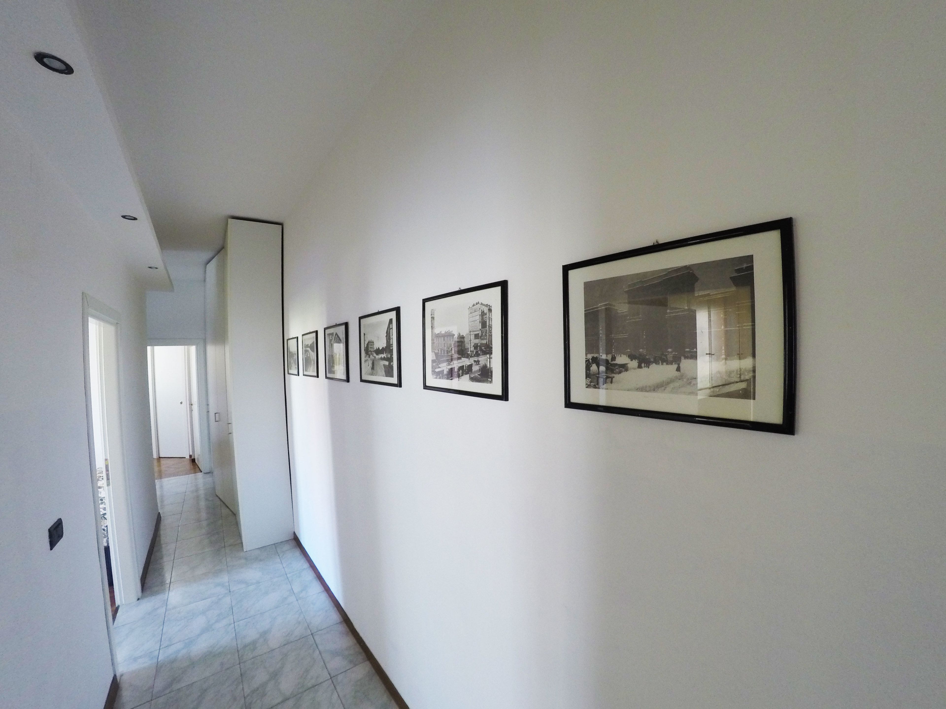 A hallway with a series of framed photographs on the wall, leading to a door at the end.