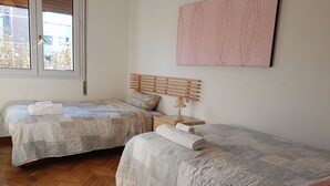 A room with two beds, wooden flooring, a bedside table with a lamp, and a window with a view of buildings. - Casa Bella Fair (Bologna)
