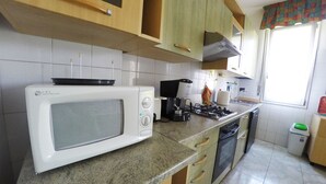 A kitchen with a white microwave, stove, and dishwasher. There are wooden cabinets and a window with curtains. - Casa Bella Fair (Bologna)