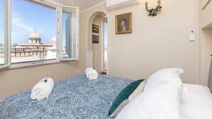 A hotel room with a bed, a window with a view of a dome structure, an air conditioning unit, and a wall-mounted light fixture. - Argentina Penthouse in the heart of the historic center (Rome)