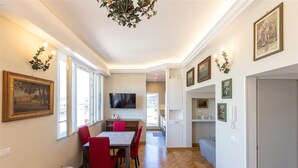 A dining area with a wooden herringbone floor, a dining table with red chairs, a TV mounted on the wall, and framed artwork on the walls. - Argentina Penthouse in the heart of the historic center (Rome)