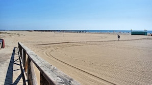 Una playa con un paseo de madera, una red de voleibol y una torre de salvavidas.