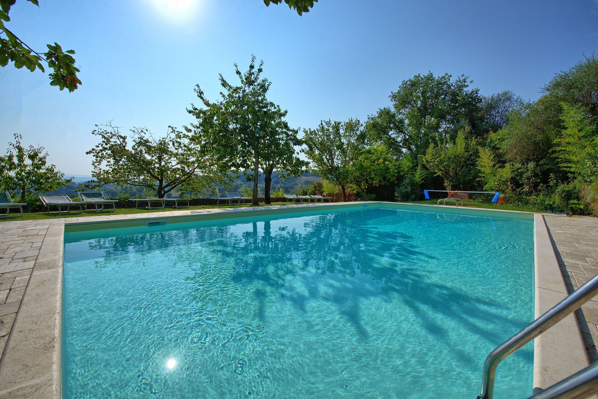 A rectangular swimming pool with clear blue water, surrounded by a paved deck.