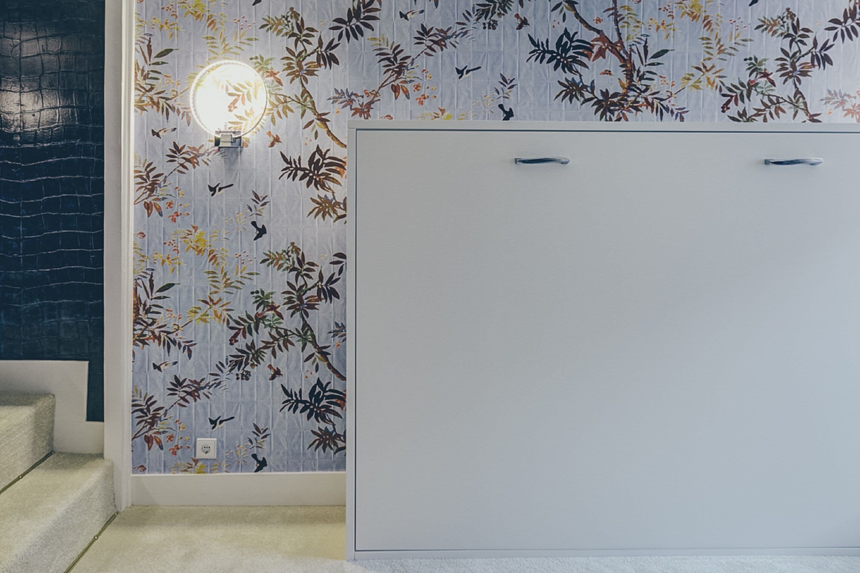 Une pièce avec un papier peint à motifs, une armoire blanche et un escalier.