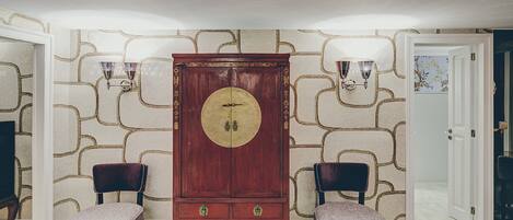 Ein Zimmer mit einem großen, hölzernen Schrank, zwei Polsterstühlen und Wandtapete mit Muster.