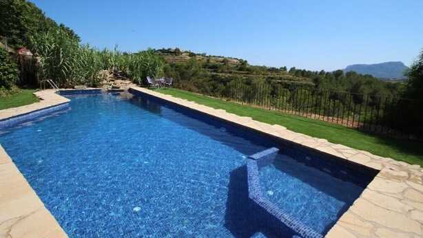 A rectangular swimming pool with clear blue water, surrounded by a stone border and a grassy area with a fence. - Rocasol - rustic finca for nature lovers in Benissa (Benissa)