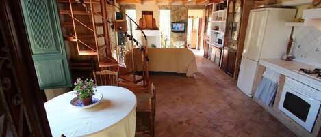 A rustic kitchen with a wooden staircase, a dining table with a potted plant, and a television in the background.