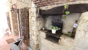 A stone fireplace with a shelf, a hanging plant, and a metal gate. - Rocasol - rustic finca for nature lovers in Benissa (Benissa)