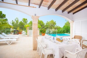 An outdoor patio with a pool, white lounge chairs, and a table set for dining.