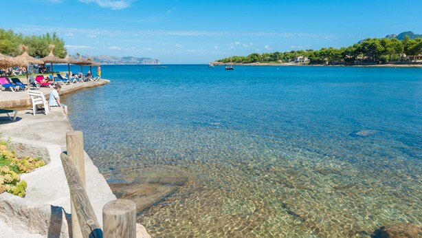 A clear waterfront with a pier, lounge chairs, and a boat in the distance. - VILLA ROMANA BONAIRE - Villa with private pool in Bonaire (Alcúdia). Free WiFi (Alcúdia)