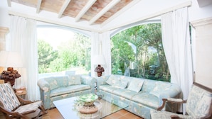 A cozy living room with a sectional sofa, a glass coffee table, and a wooden rocking chair. - VILLA ROMANA BONAIRE - Villa with private pool in Bonaire (Alcúdia). Free WiFi (Alcúdia)