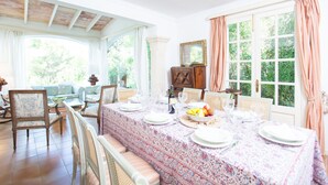 A dining area with a long table set for six, surrounded by chairs, a sofa, and a window with curtains. - VILLA ROMANA BONAIRE - Villa with private pool in Bonaire (Alcúdia). Free WiFi (Alcúdia)