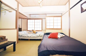 Habitación compacta con dos camas, una mesita pequeña y aire acondicionado instalado en la pared.