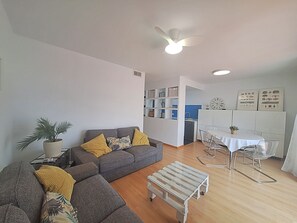 Una sala de estar moderna con un sofá seccional gris, una pequeña mesa de centro de madera y un comedor con una mesa y sillas blancas.
