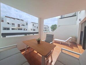 A balcony with a wooden table, two chairs, a potted plant, and a lounge chair.