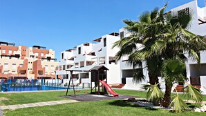 A playground with a slide and swings, surrounded by palm trees and a pool. - AL 230 - Apartment near the beach (Vera playa)