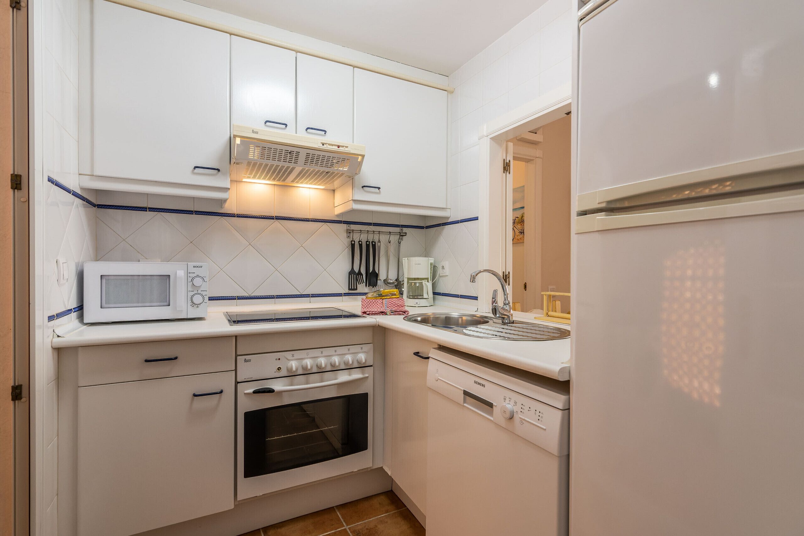 Una cocina compacta con armarios blancos, microondas, estufa, lavavajillas y refrigerador.