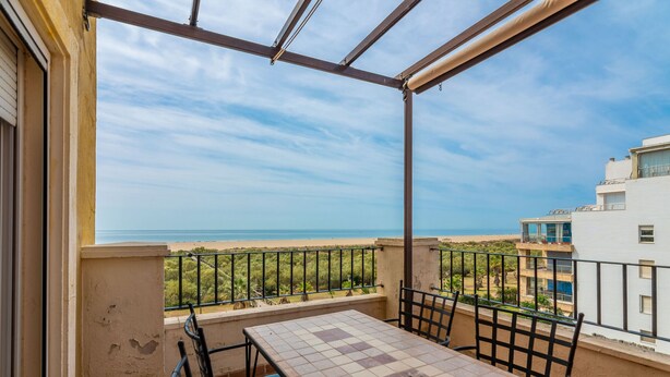 Un balcon avec une table et des chaises, donnant sur une plage et un immeuble.
