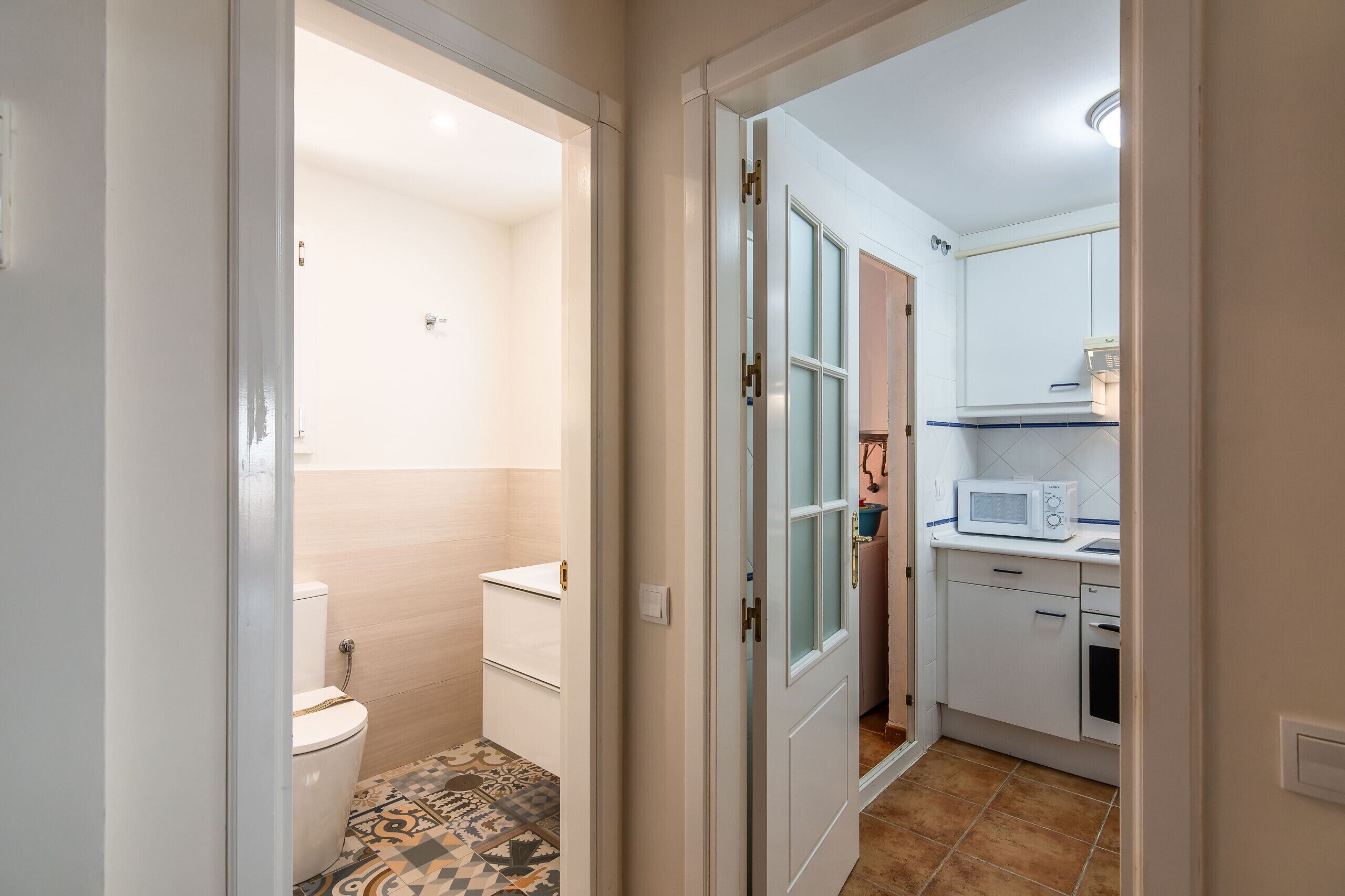 Un baño compacto con inodoro y lavamanos, una kitchenette pequeña con microondas, y un piso estampado.