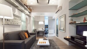 Ein modernes Wohnzimmer mit einer Couch, einem Couchtisch und einem Fernseher. Im Hintergrund befindet sich ein Essbereich mit Tisch und Stühlen.