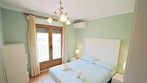 A bedroom with a bed, nightstands, a lamp, a ceiling fan, a window with curtains, and an air conditioning unit. - Marques - holiday home with private swimming pool in Benitachell (Benitachell)