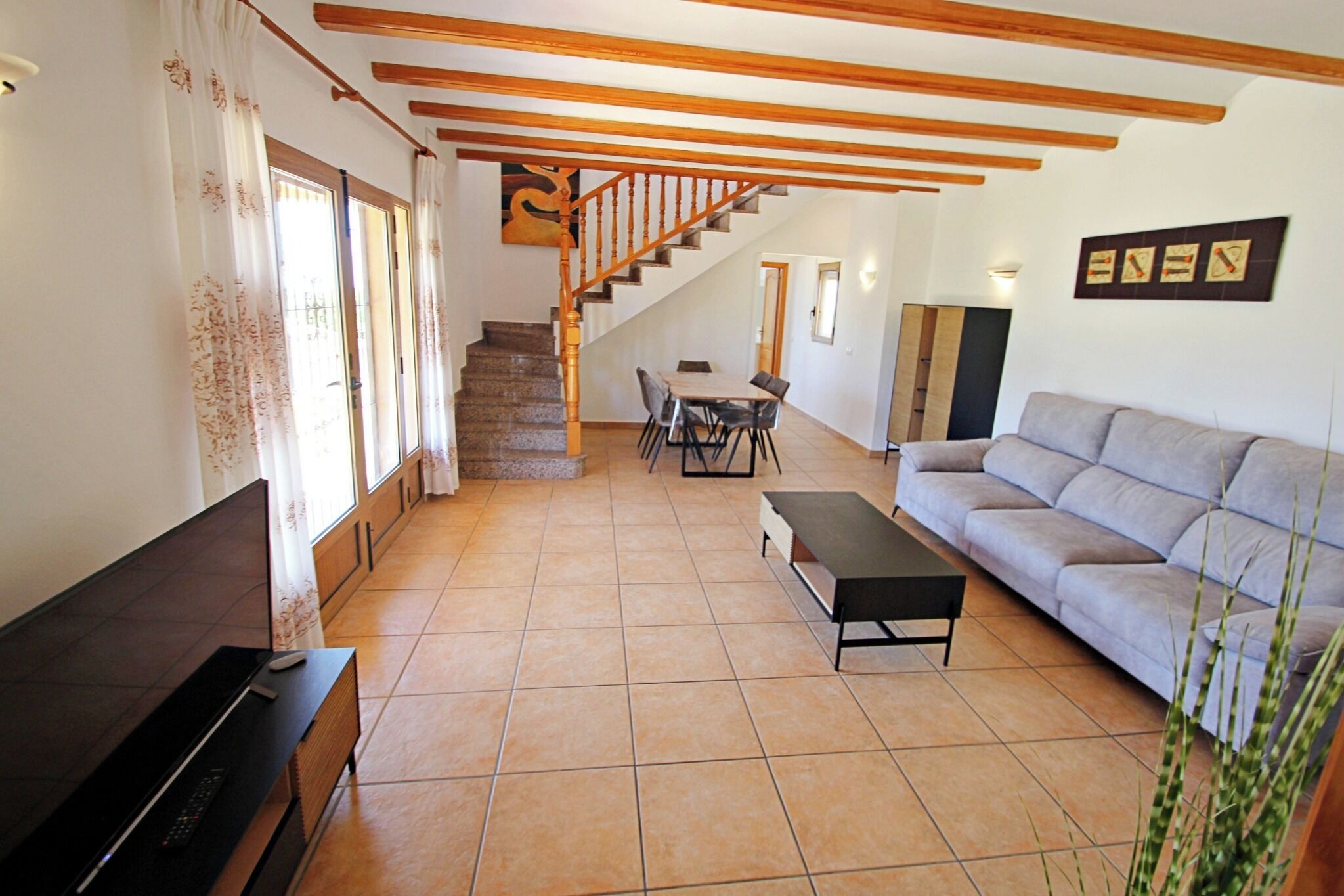A living room with a sofa, a TV, a dining table, and a staircase leading to another level.