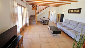A living room with a sofa, a TV, a dining table, and a staircase leading to another level. - Marques - holiday home with private swimming pool in Benitachell (Benitachell)