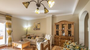 Uma sala de estar com sofá, cadeiras, mesa de centro, armário e lustre.
