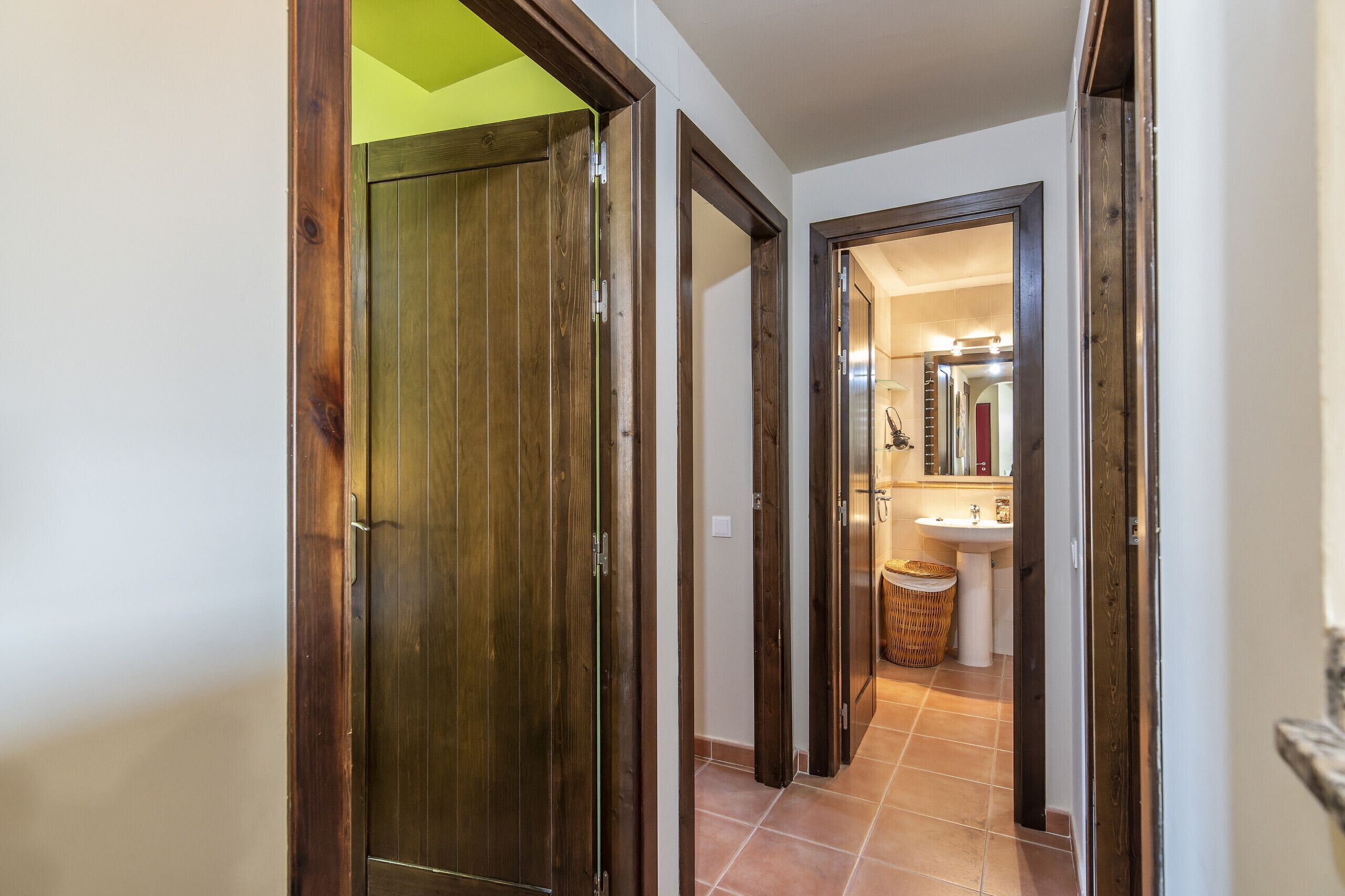 Un pasillo con puertas de madera que dan a un baño con lavabo y espejo.