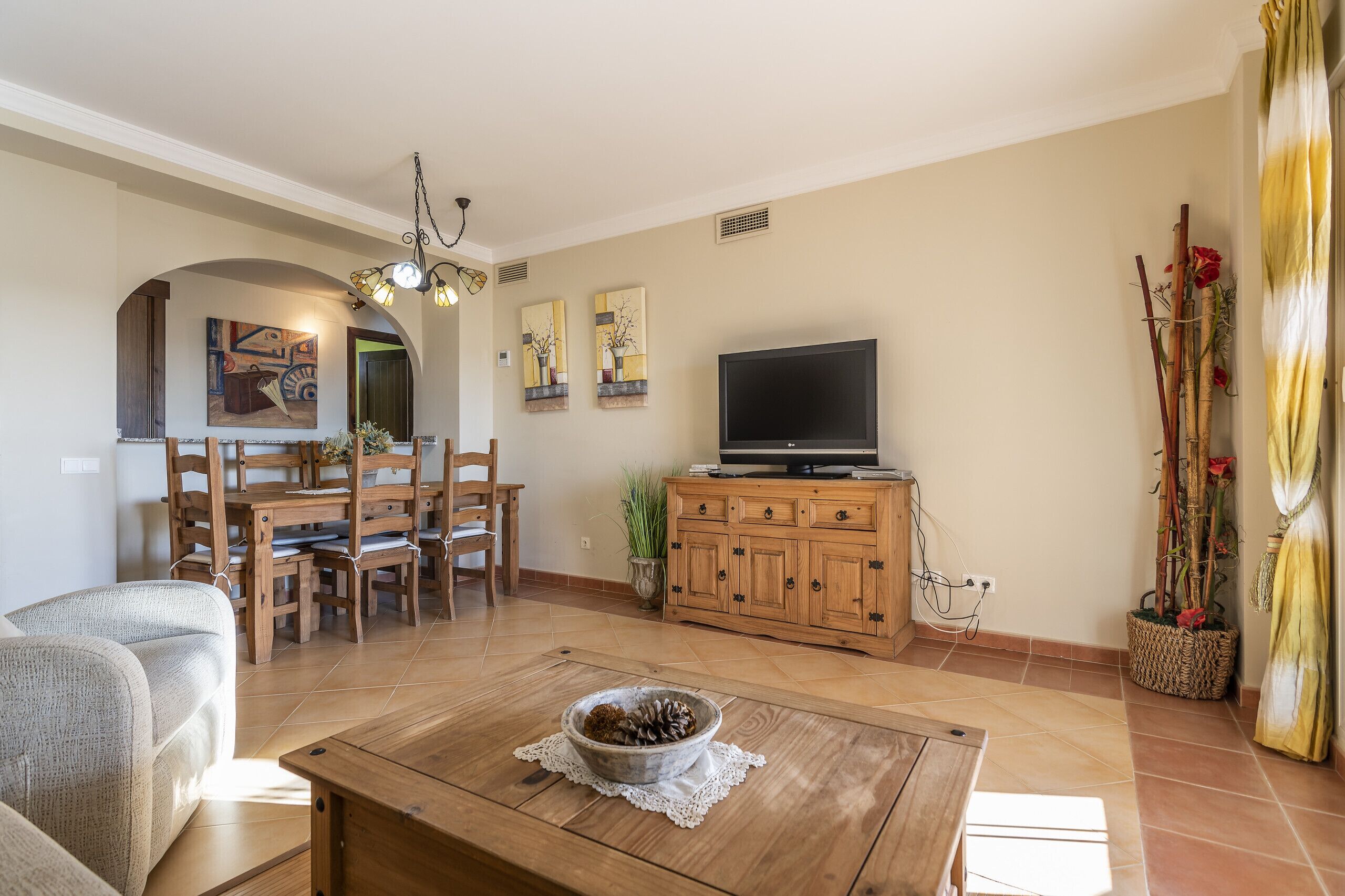 Una sala de estar con una mesa de comedor de madera, un sofá, un televisor y un mueble de almacenamiento.
