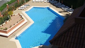 Piscina retangular com um deck ladrilhado ao redor, equipada com várias espreguiçadeiras e guarda-sóis.