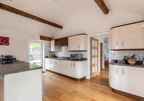 Kitchen with central island, white cabinetry, and wooden ceiling beam, featuring a large window and door to adjacent room.