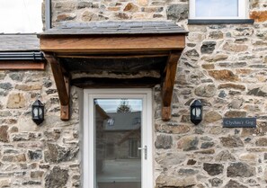 Experience the rustic charm of Clychau'The Gog, a traditional stone building with a wooden overhang and lantern-style lights.