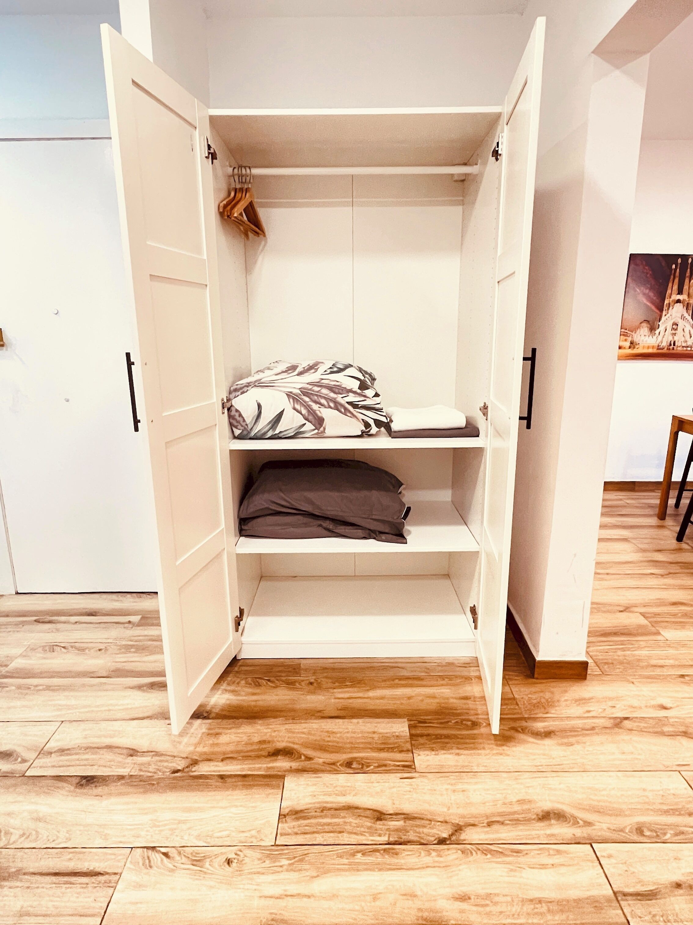 Ein weißer Kleiderschrank mit geöffneten Türen, der Regale und Platz zum Aufhängen zeigt.