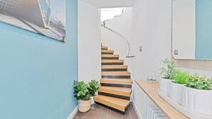 En modern trappa med trästeg och ett glasräcke, som leder upp till en liten plattform med en vit vägg och en liten krukväxt.