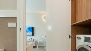 A modern room with a washing machine, a television on the wall, and a small seating area with a chair and table.