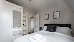 A bedroom with a large bed, a wardrobe, and two wall-mounted pictures. - Comfy 2 Bed Flat (QCE) (Greater London)