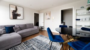 A modern living room with a grey sofa, blue chairs, a dining table, and a patterned rug. - Comfy 2 Bed Flat (QCE) (Greater London)