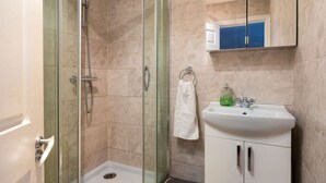 A bathroom with a glass-enclosed shower, a white sink, and a mirror above the sink. - Comfy 2 Bed Flat (QCE) (Greater London)