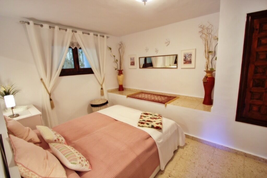 Une chambre à coucher comprenant un lit, une table de chevet, une fenêtre avec des rideaux, un miroir et des éléments de décoration fixés au mur.