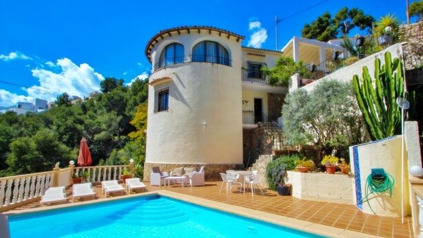 Un área de piscina con sillones de descanso y un edificio blanco con una torre redondeada.