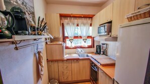 Cocina compacta con armarios de madera, microondas, lavamanos y un pequeño cubo de basura.