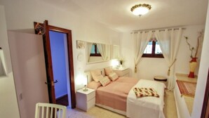 Un dormitorio con cama, mesitas de noche, un espejo, una ventana con cortinas y una puerta.