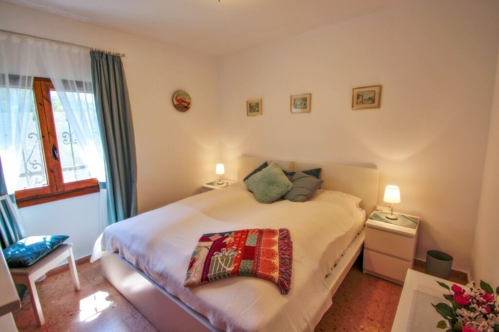 A neatly arranged bedroom with a bed, bedside tables, a chair, and a window with curtains.