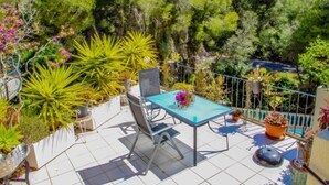 Una terraza con mesa y sillas, rodeada de macetas y árboles.